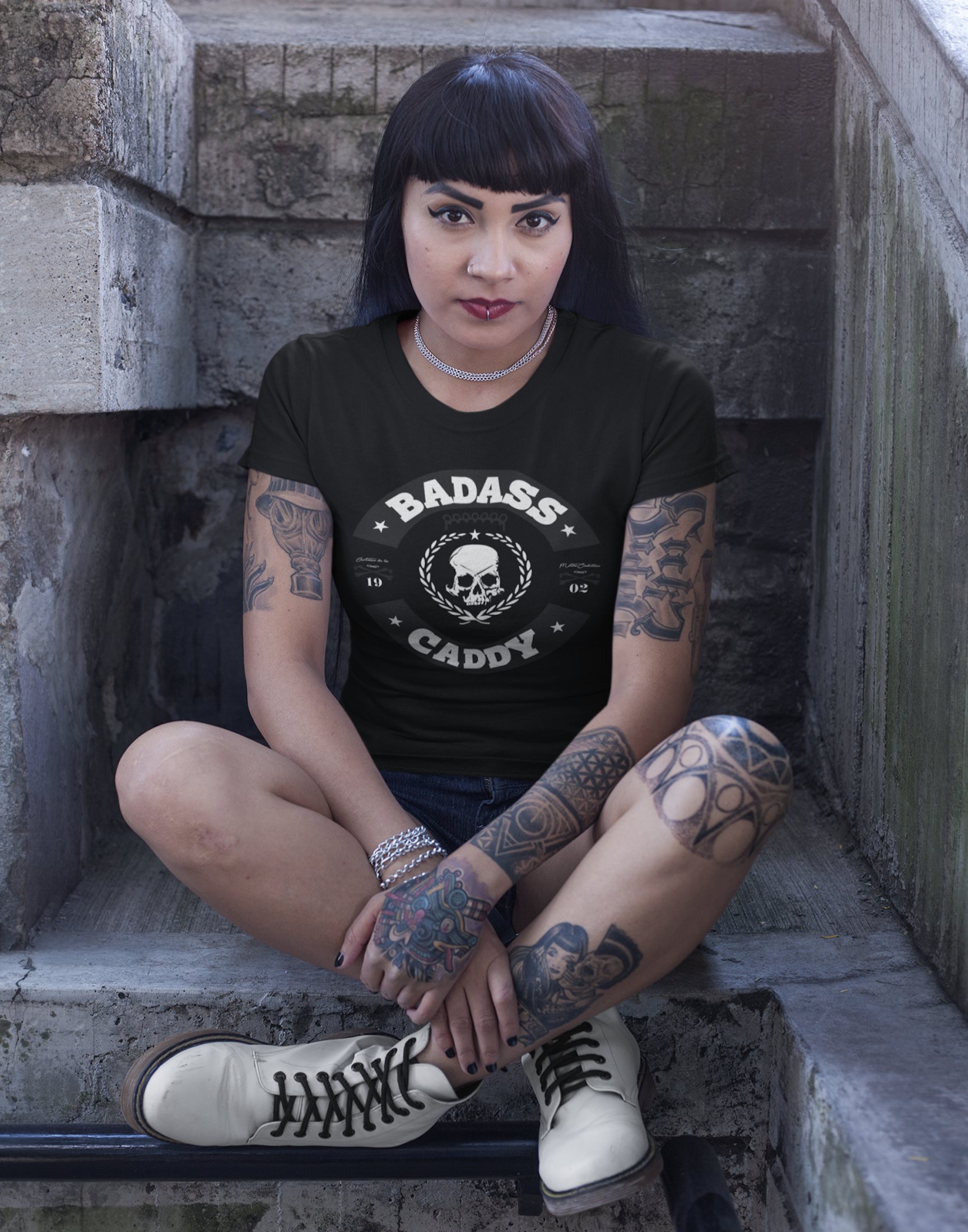 Woman wearing a black t-shirt with 'BADASS CADDY' design, sitting on stone steps.
