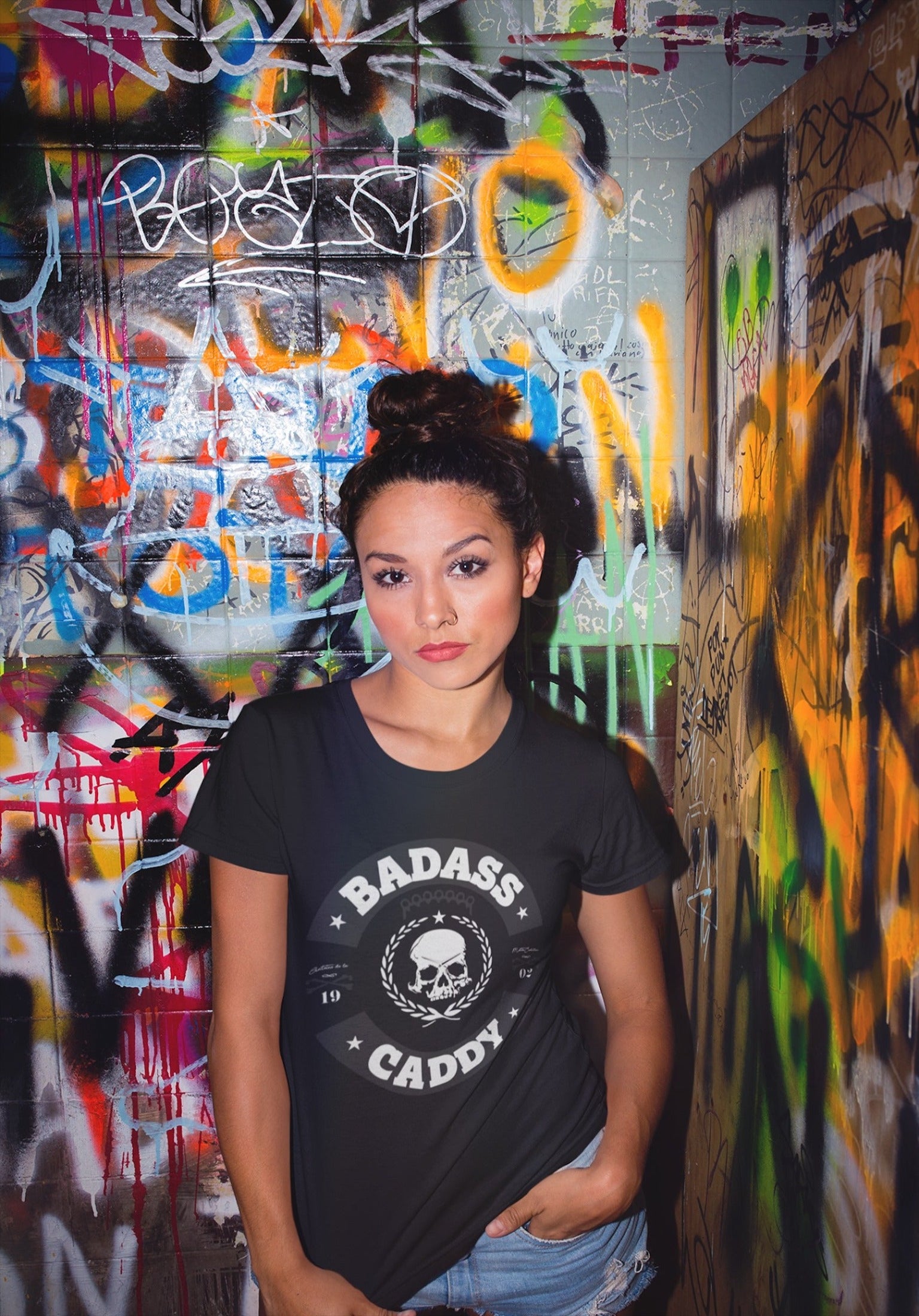 Woman_wearing_a_black_t-shirt_with_BADASS_CADDY_design_with_graffiti_wall.